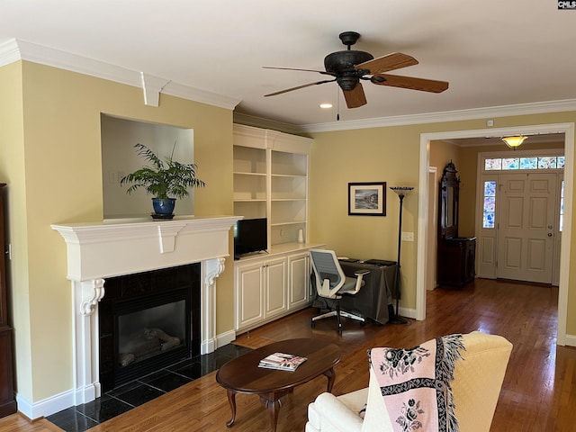 living room featuring crown molding, dark wood finished floors, a ceiling fan, baseboards, and a fireplace with flush hearth
