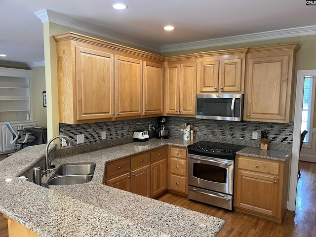 kitchen with appliances with stainless steel finishes, a sink, a peninsula, wood finished floors, and ornamental molding