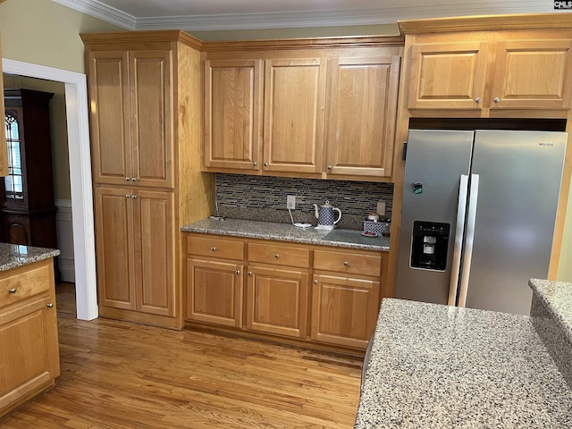 kitchen with backsplash, light stone countertops, light wood finished floors, stainless steel fridge, and ornamental molding