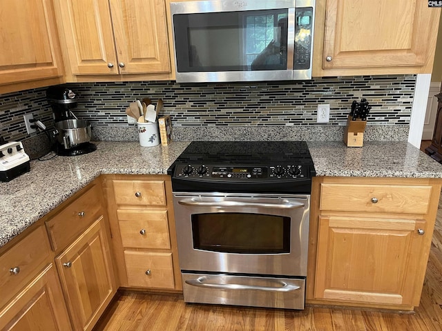 kitchen with light stone counters, appliances with stainless steel finishes, tasteful backsplash, and light wood-style flooring