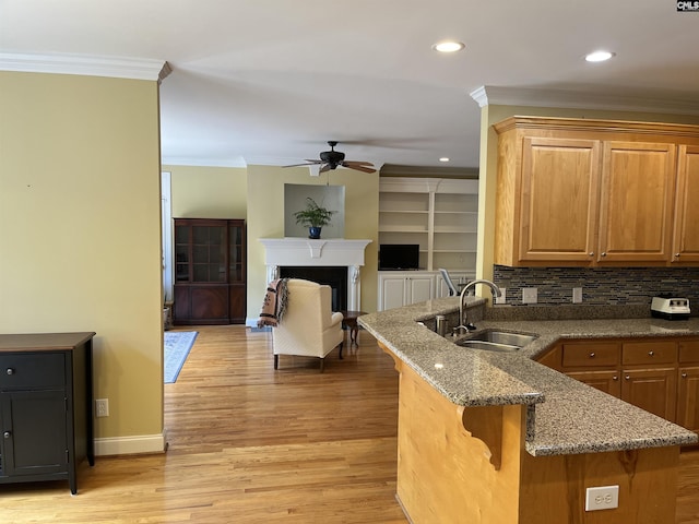 kitchen with a sink, dark stone counters, a ceiling fan, a peninsula, and ornamental molding