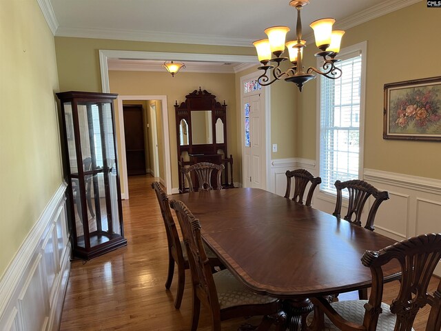 dining area featuring ornamental molding, wainscoting, wood finished floors, and a notable chandelier