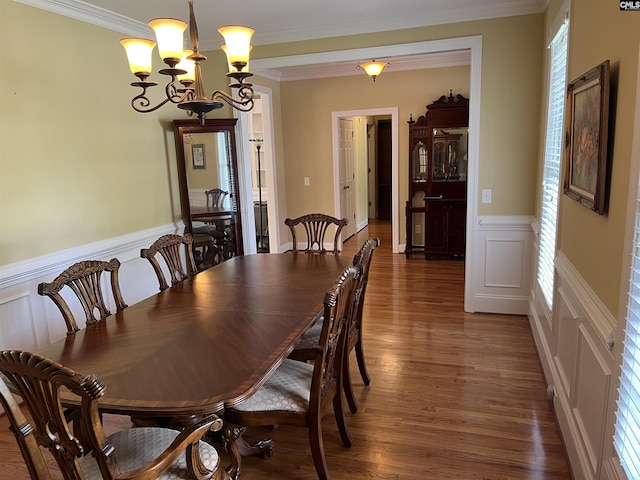 dining area featuring crown molding, wainscoting, wood finished floors, an inviting chandelier, and a decorative wall