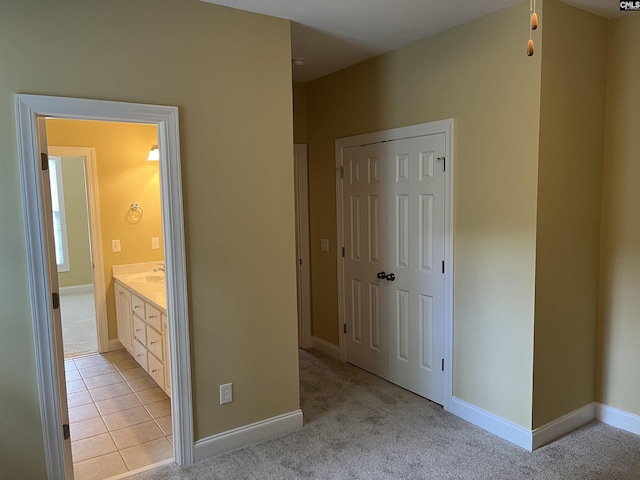 unfurnished bedroom with baseboards, light carpet, a sink, and a closet