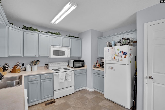 kitchen featuring gray cabinets, visible vents, a sink, light countertops, and white appliances