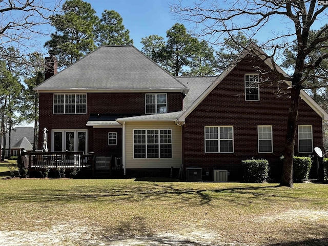 back of house with central AC, brick siding, a deck, a chimney, and a lawn