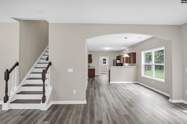 interior space featuring arched walkways, baseboards, stairs, and wood finished floors