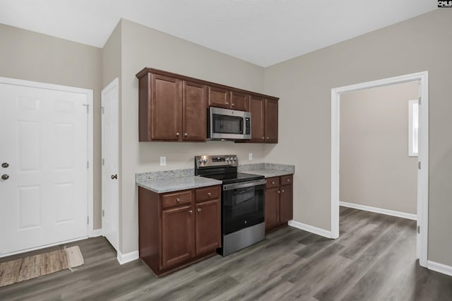 kitchen with light stone countertops, baseboards, appliances with stainless steel finishes, and dark wood-type flooring