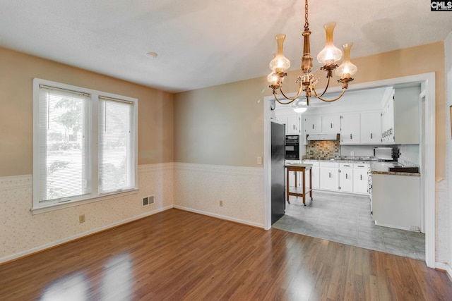 unfurnished dining area with an inviting chandelier, wainscoting, wallpapered walls, wood finished floors, and visible vents
