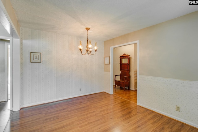 unfurnished dining area featuring baseboards, wallpapered walls, a notable chandelier, and wood finished floors