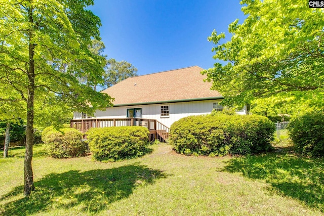 rear view of house with a lawn, fence, a wooden deck, and a shingled roof