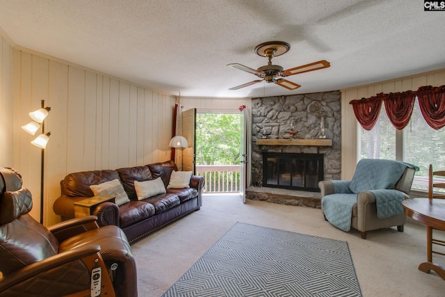 carpeted living area featuring a stone fireplace, a ceiling fan, a textured ceiling, and wooden walls