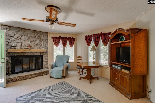living area with a fireplace, ceiling fan, wooden walls, light colored carpet, and a textured ceiling