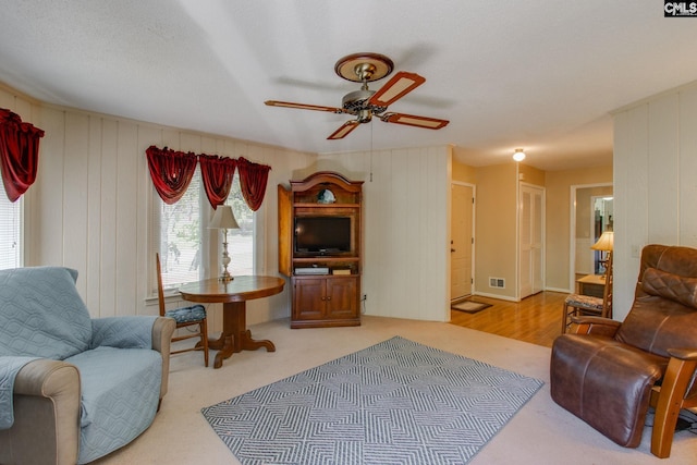 living room featuring a ceiling fan, wood walls, and visible vents