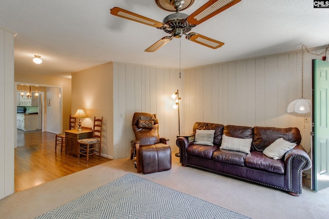 living room featuring a textured ceiling, carpet, and ceiling fan with notable chandelier