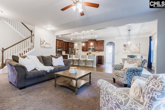 living area with stairs, arched walkways, and a ceiling fan
