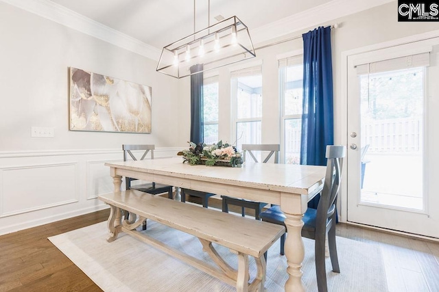 dining area with crown molding, wood finished floors, and a wainscoted wall