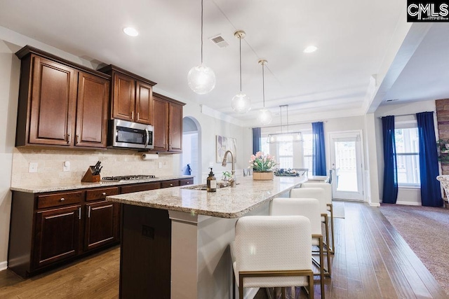 kitchen featuring appliances with stainless steel finishes, light stone counters, a sink, arched walkways, and visible vents