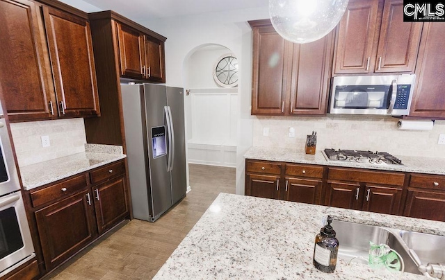 kitchen featuring arched walkways, tasteful backsplash, light stone countertops, wood finished floors, and stainless steel appliances