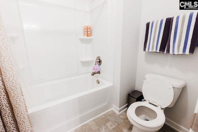 full bath featuring baseboards, stone finish flooring, shower / bath combination with curtain, and toilet