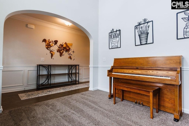 sitting room featuring crown molding, arched walkways, carpet, and wainscoting