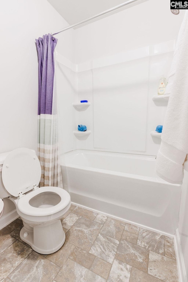 bathroom featuring stone tile flooring, shower / bath combo, and toilet