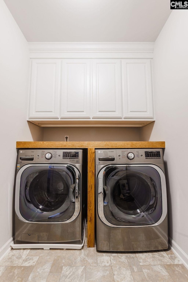 laundry room featuring cabinet space, baseboards, stone finish floor, and washer and clothes dryer