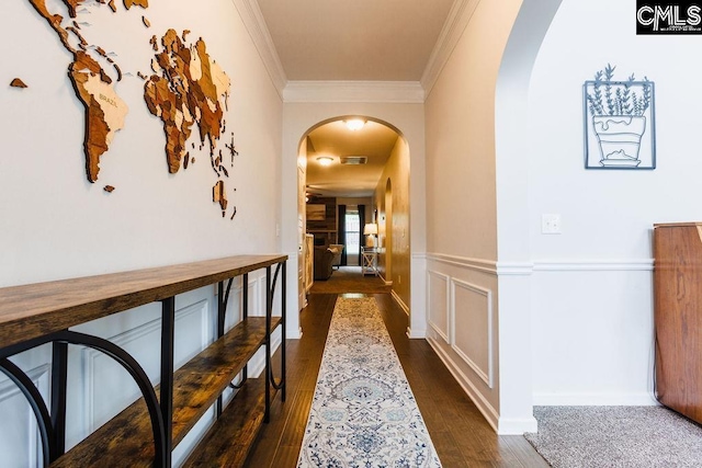 hallway with arched walkways, ornamental molding, a wainscoted wall, and dark wood finished floors