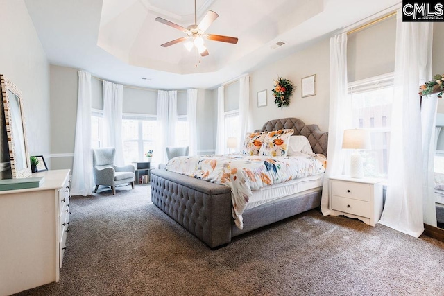 carpeted bedroom with a ceiling fan, a tray ceiling, and visible vents