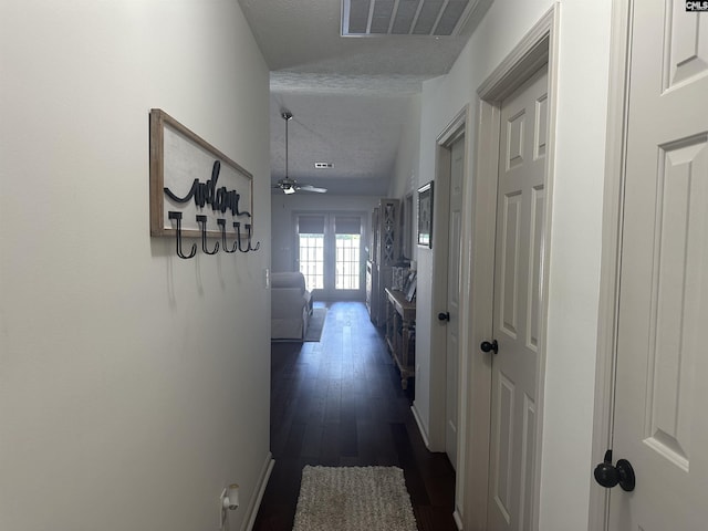 hallway with dark wood finished floors, a textured ceiling, and visible vents