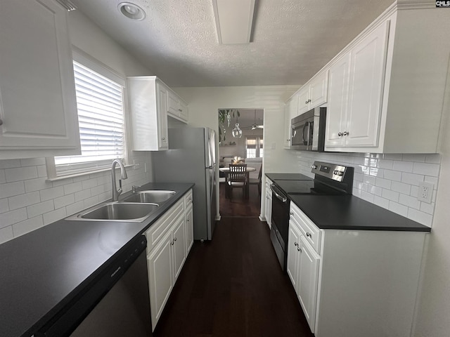 kitchen featuring a textured ceiling, dark countertops, a sink, white cabinets, and stainless steel appliances