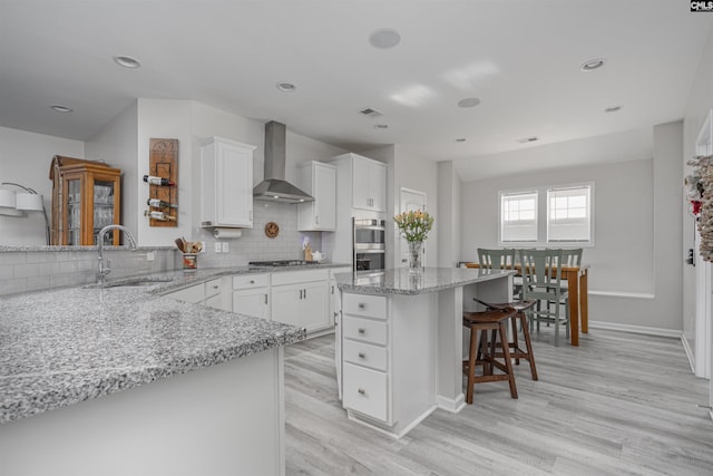 kitchen featuring wall chimney range hood, a kitchen breakfast bar, appliances with stainless steel finishes, a sink, and light wood-style flooring