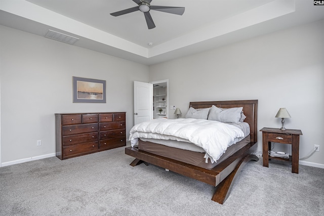 carpeted bedroom with a ceiling fan, baseboards, visible vents, and a tray ceiling