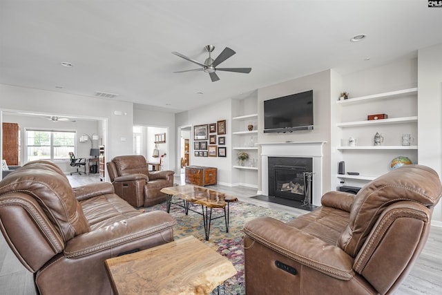 living room with a ceiling fan, visible vents, a fireplace with flush hearth, wood finished floors, and built in shelves
