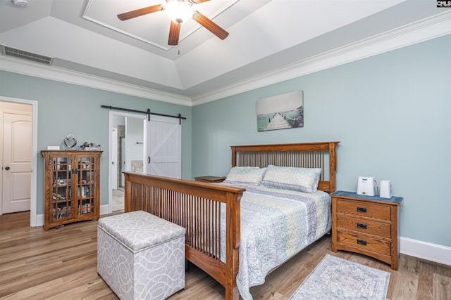 bedroom featuring visible vents, a barn door, a raised ceiling, ornamental molding, and light wood-style flooring