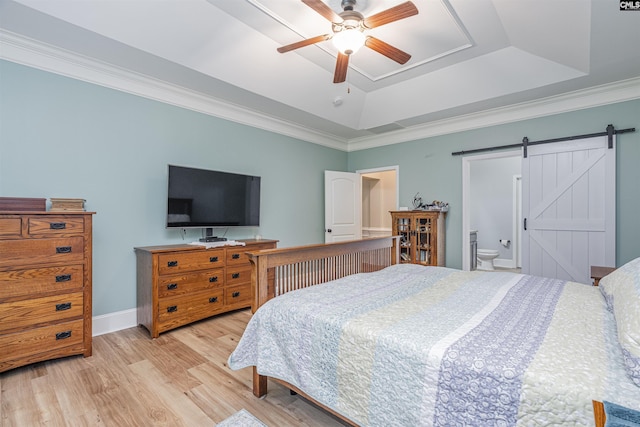 bedroom featuring crown molding, wood finished floors, a barn door, baseboards, and a tray ceiling