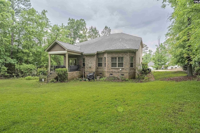 back of property featuring a yard, crawl space, brick siding, and roof with shingles