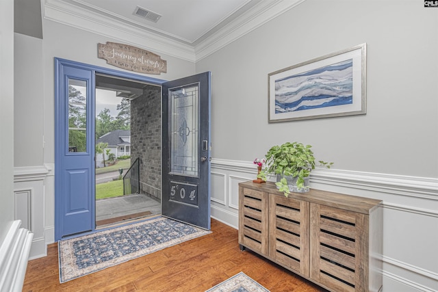 foyer entrance with visible vents, crown molding, wainscoting, wood finished floors, and a decorative wall