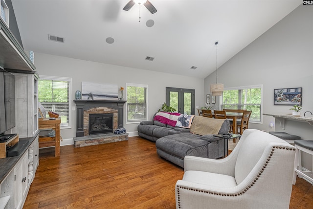 living room with a healthy amount of sunlight, a ceiling fan, a stone fireplace, visible vents, and wood finished floors