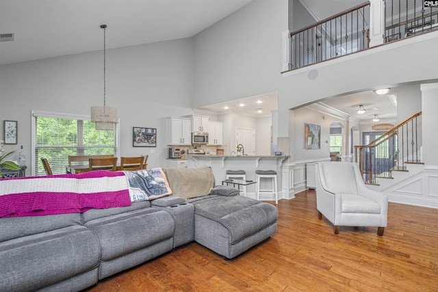 living room with light wood-type flooring, arched walkways, stairs, and high vaulted ceiling