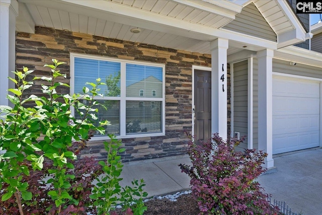 view of exterior entry featuring a porch, a garage, and stone siding