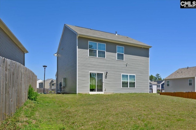 rear view of house featuring fence and a lawn