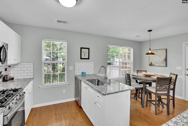 kitchen featuring appliances with stainless steel finishes, a sink, light wood-style floors, a peninsula, and visible vents