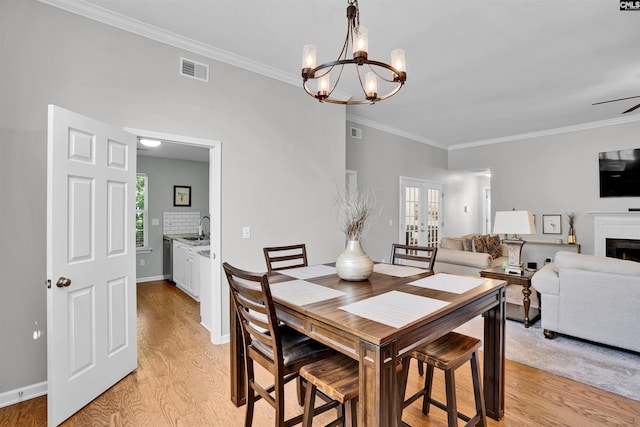 dining room with light wood-style floors, crown molding, a fireplace, and visible vents