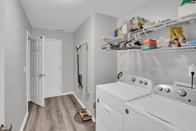 clothes washing area with laundry area, a textured ceiling, separate washer and dryer, and light wood-type flooring