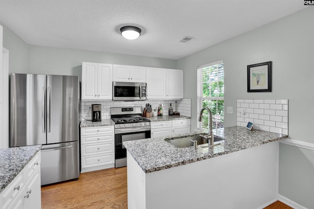 kitchen with visible vents, decorative backsplash, a peninsula, a sink, and stainless steel appliances