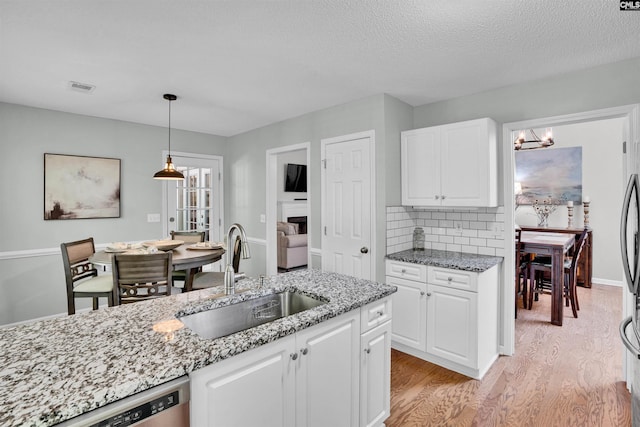 kitchen featuring visible vents, light stone countertops, light wood-style floors, white cabinetry, and a sink