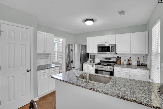 kitchen with visible vents, appliances with stainless steel finishes, a sink, stone countertops, and white cabinetry