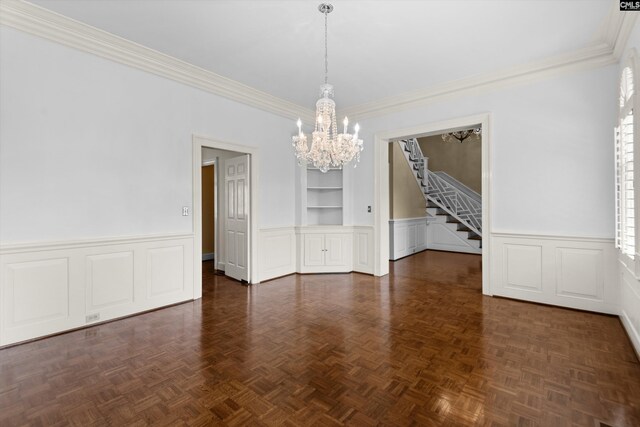 unfurnished dining area featuring a notable chandelier, built in features, ornamental molding, and stairway