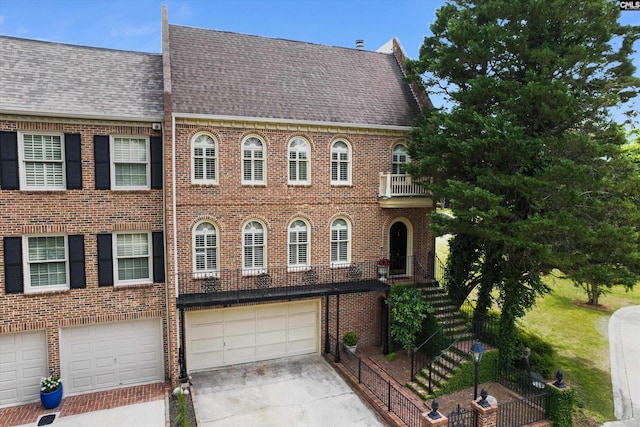 view of front facade featuring driveway, a garage, brick siding, a balcony, and a shingled roof
